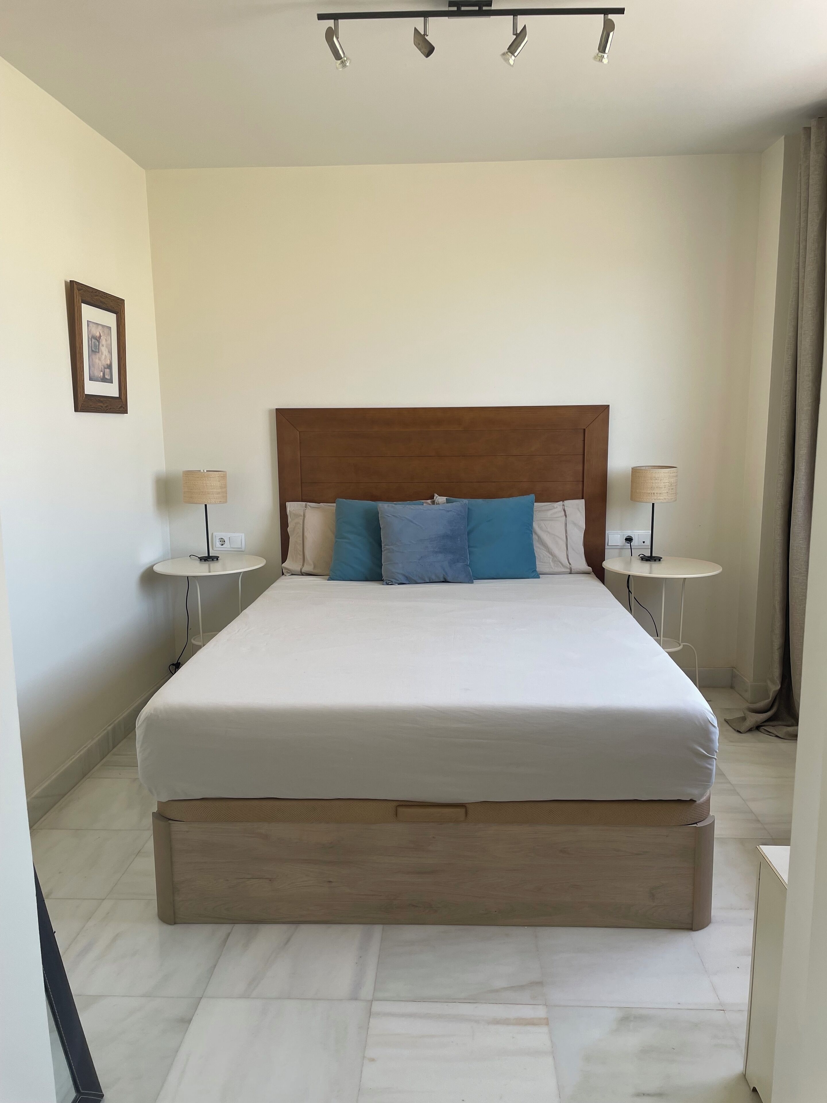 Un dormitorio ordenado con una cama grande, dos mesitas de noche y una lámpara en el techo.