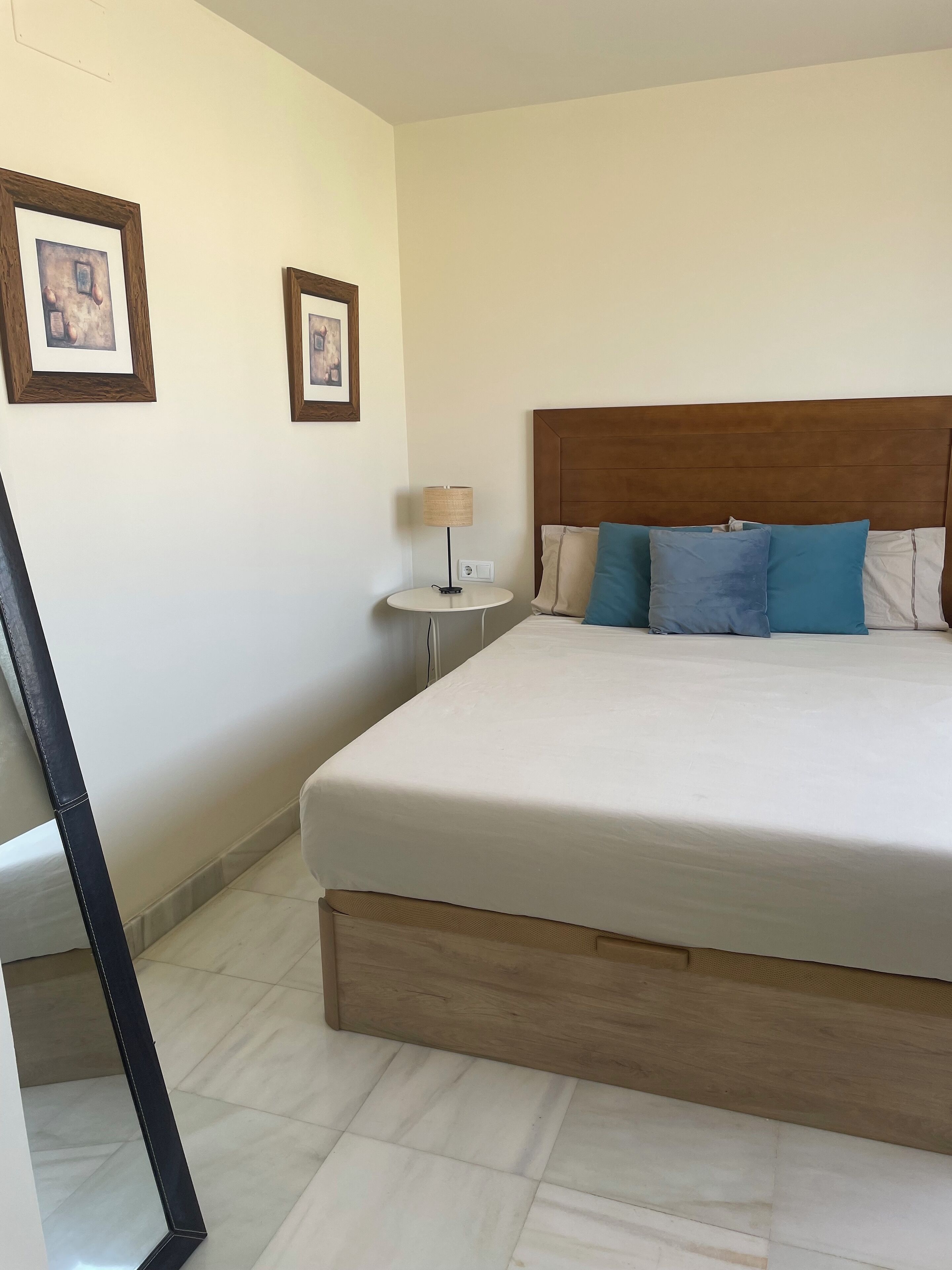 A neatly arranged hotel room with a large bed, a small bedside table, and two framed pictures on the wall.