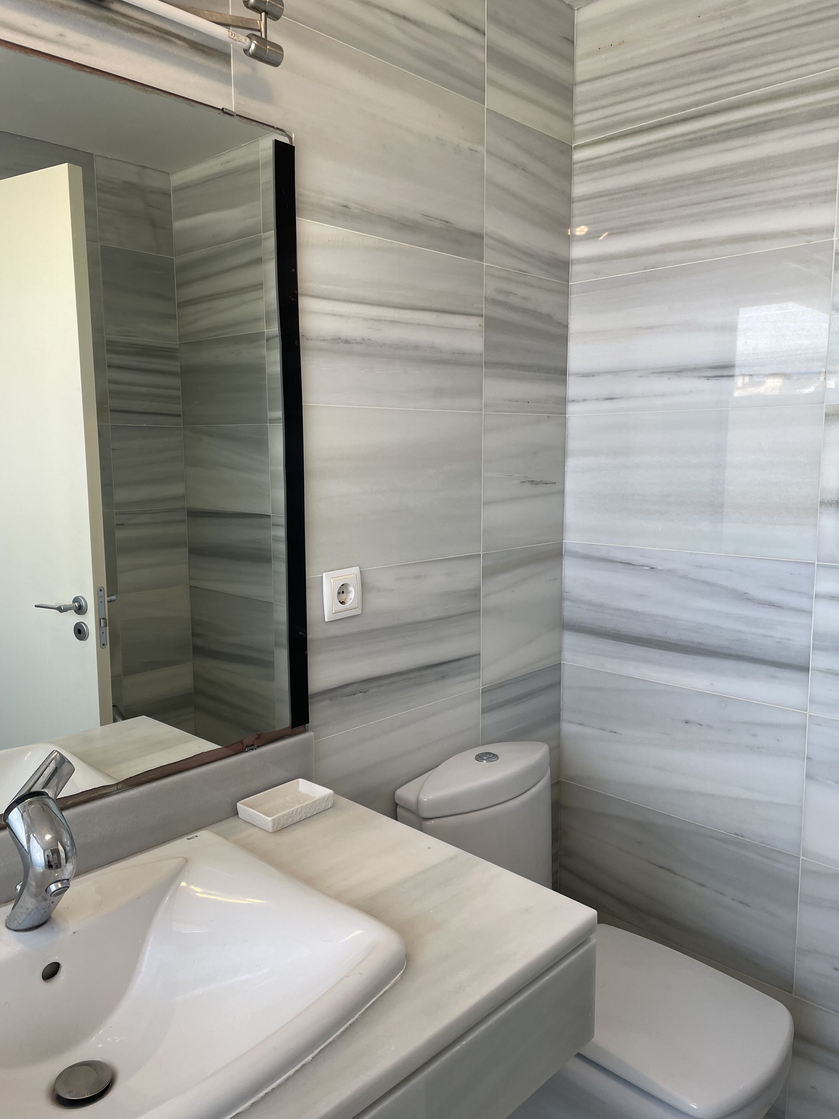 A bathroom with a white sink, mirror, and toilet against marble walls.