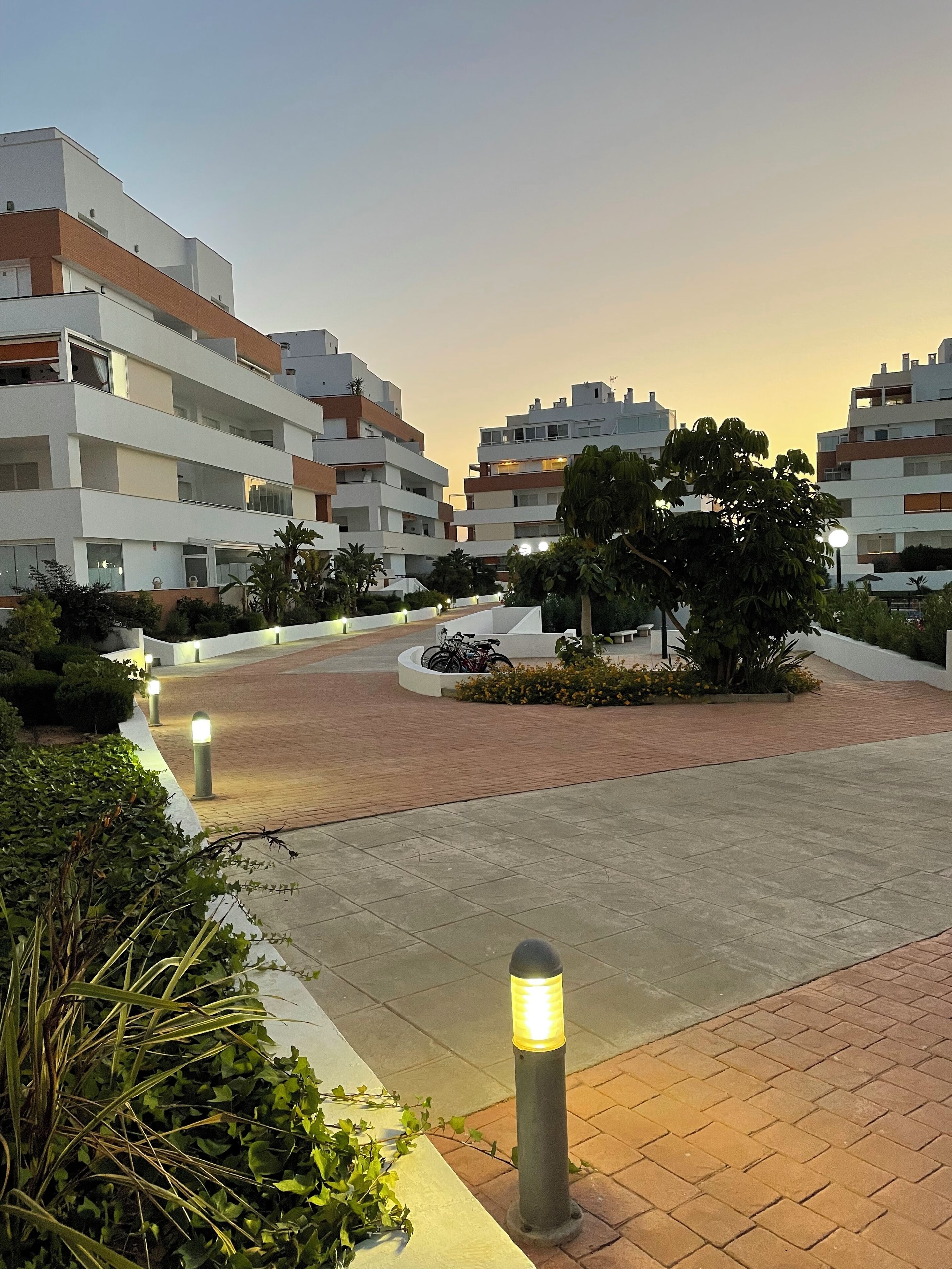 Een modern wooncomplex met meerdere appartementencomplexen, verharde paden en aangelegde groene zones met planten en bomen.