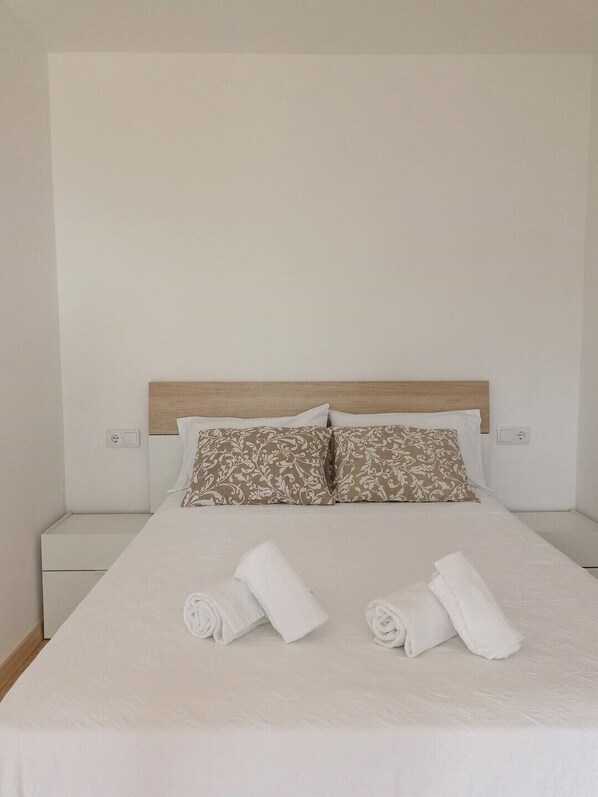 A neatly made bed with two pillows and two rolled towels on a white bedspread. - Casal do Crego (O Grove)