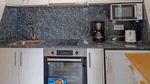 Eine kleine Küche mit weißen Schränken, einer eingebauten Mikrowelle, einer Kaffeemaschine, einem Toaster und einem Geschirrspüler.