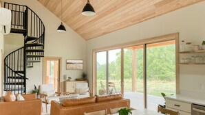A spacious living area with a wooden staircase, a dining table, and a large window offering a view of the outdoors. - Cabin Retreat at Stillhouse Farm NEW (Lexington)