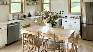 A kitchen with wooden cabinets, a dining table with chairs, a refrigerator, and a window with a view of greenery. - Cabin Retreat at Stillhouse Farm NEW (Lexington)