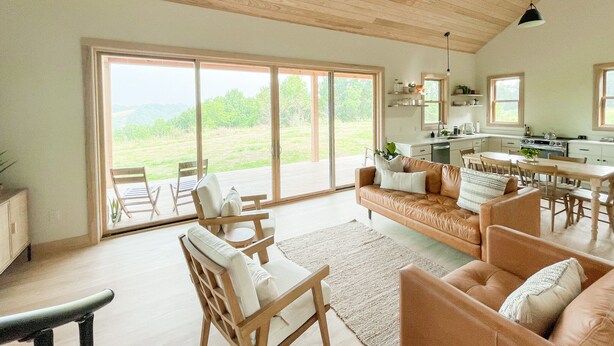 A spacious living area with a large sliding glass door leading to a deck, a kitchen with white cabinets, and a dining area with wooden furniture. - Cabin Retreat at Stillhouse Farm NEW (Lexington)