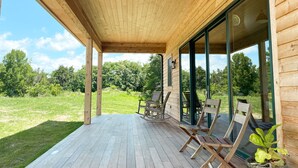 A wooden deck with a covered area, outdoor furniture, and a view of a green landscape. - Cabin Retreat at Stillhouse Farm NEW (Lexington)