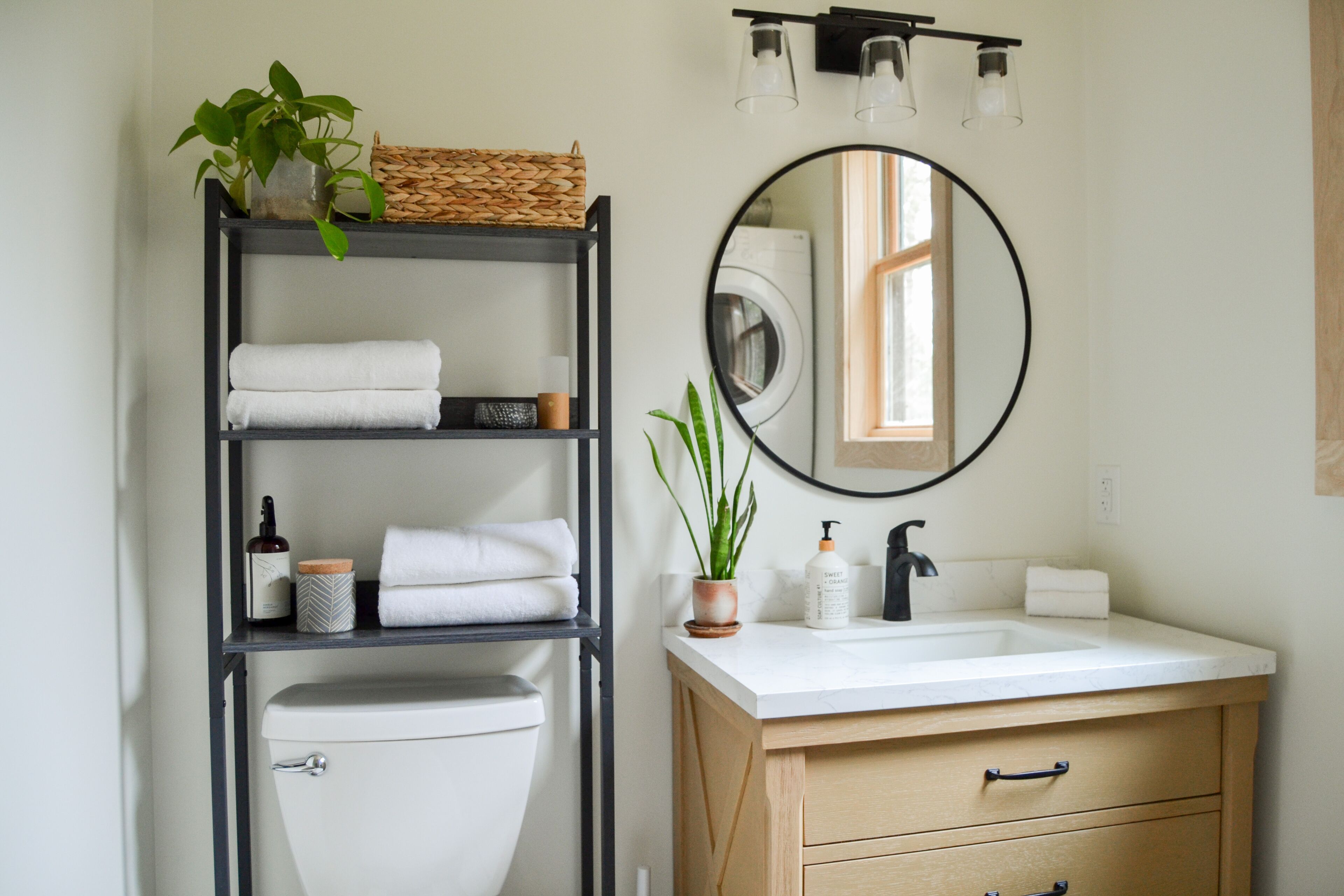 A modern bathroom with a toilet, a sink, a mirror, and a shelf with towels and toiletries.