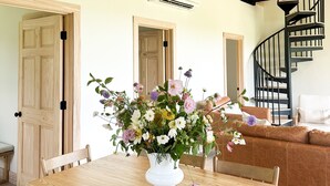 A dining area with a wooden table and chairs, a flower vase, and a black spiral staircase in the background. - Cabin Retreat at Stillhouse Farm NEW (Lexington)