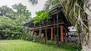 A wooden structure with a covered porch, surrounded by lush greenery and a parked car. - The Treehouse Studio apartments with a large rooftop terrace. (Aburi-South)