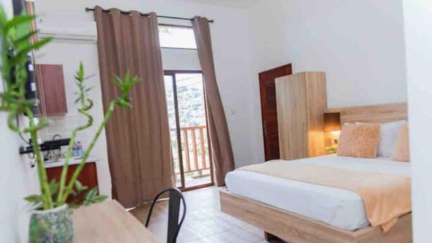 A bedroom with a wooden bed, a desk with a chair, a potted plant, and a sliding door leading to a balcony. - The Treehouse Studio apartments with a large rooftop terrace. (Aburi-South)