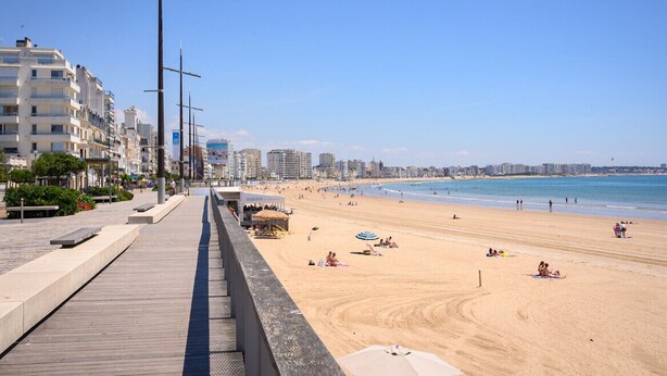A beach with a wooden promenade, beach umbrellas, and people relaxing.