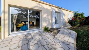 A house with a stone patio, a sliding glass door, and a small garden with red flowers.