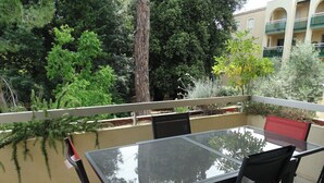 A balcony with a glass table and chairs, surrounded by greenery and a building in the background. - Spacious cocoon with two terraces (Montpellier)