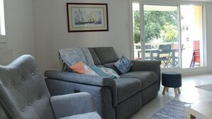 A living room with a grey sofa, a chair, a framed picture on the wall, and a view of an outdoor patio with chairs and a table. - Spacious cocoon with two terraces (Montpellier)