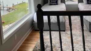 A bedroom with a view of the sea, a balcony railing, and a bed with pillows. - Bayou on the Bay (Stevensville)