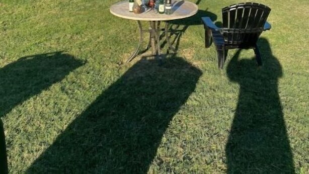A thatched umbrella table with a chair and a bottle of wine on a grassy area by the water. - Bayou on the Bay (Stevensville)