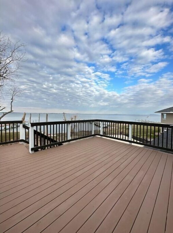 A wooden deck with a black railing, overlooking a body of water and a grassy area.