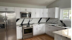 A modern kitchen with white cabinets, stainless steel appliances, and a marble backsplash. - Bayou on the Bay (Stevensville)