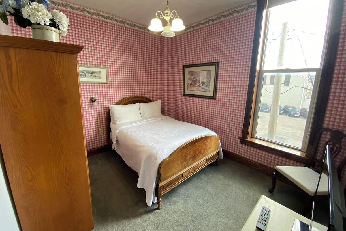 A bedroom with a wooden bed, a wooden dresser, a chair, and a window with a view of parked cars.