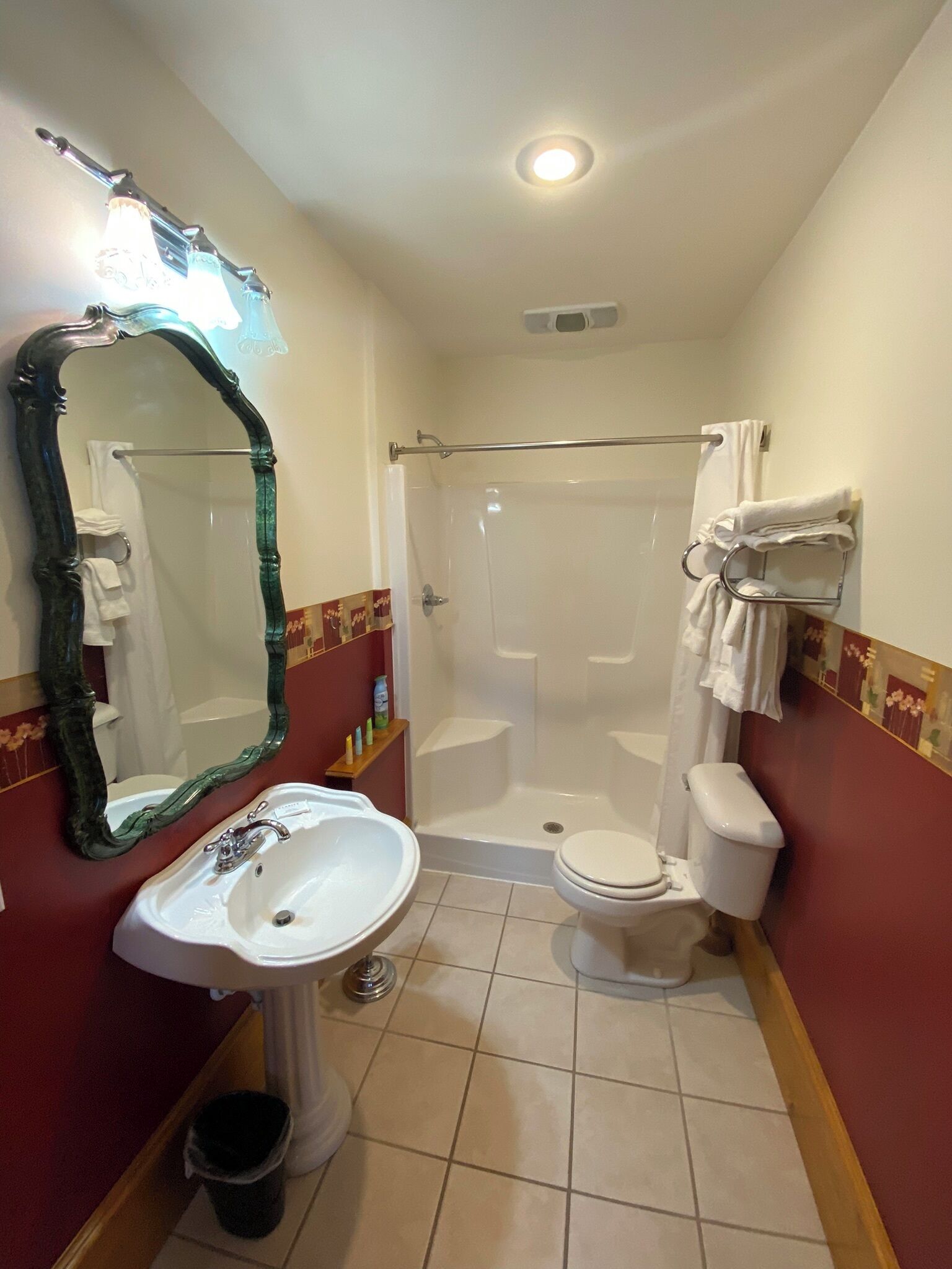 A bathroom with a white sink, toilet, and shower. There is a large mirror with an ornate frame, and towels are hung on a rack.