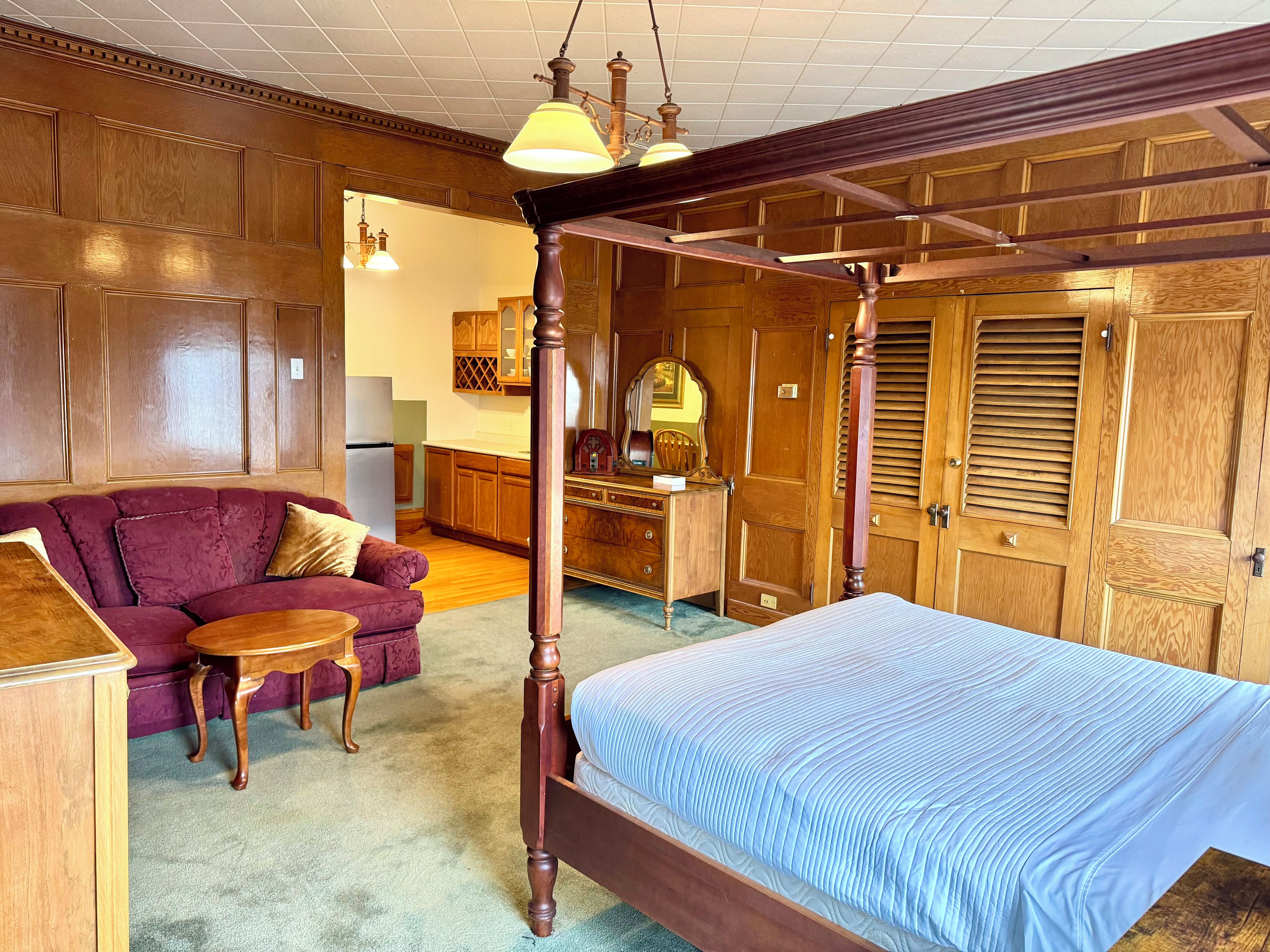 Un dormitorio con cama con dosel, armario de madera y un rincón de descanso con sofá y mesa.