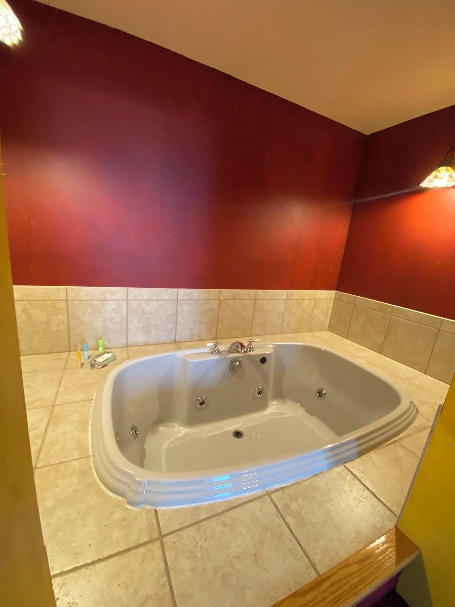 A bathroom with a freestanding bathtub, beige tiled floor, and red walls.