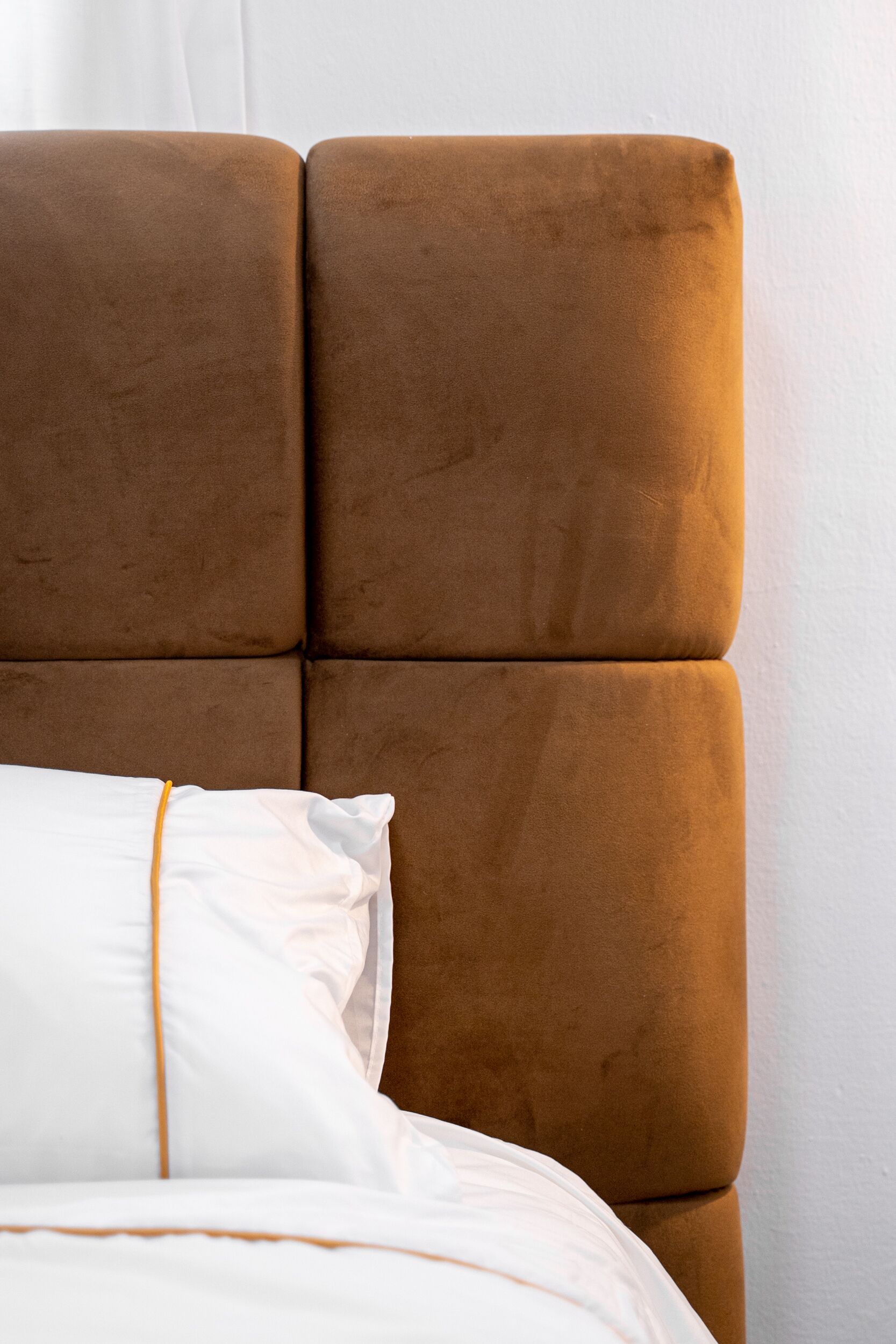 A bed with a brown upholstered headboard and white bedding.