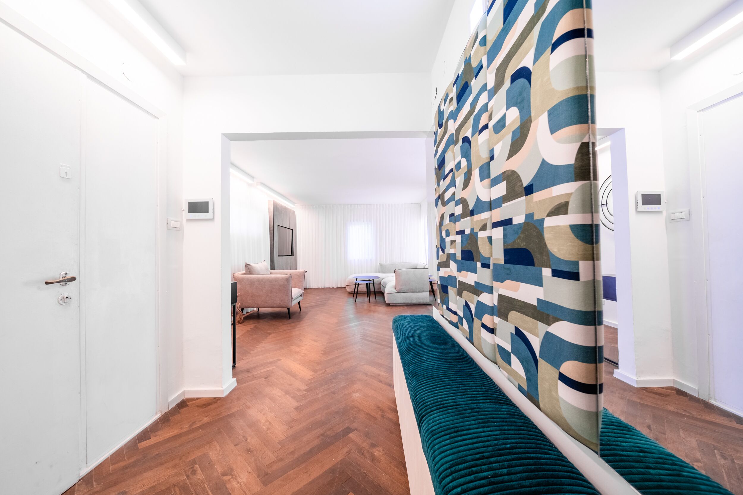 A modern interior with a herringbone wood floor, a teal bench, and a patterned wall.