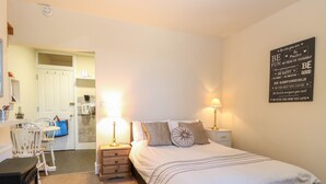 Une chambre à coucher avec un lit, des lampes de chevet, un élément décoratif mural, une chaise, une petite table et un four à micro-ondes à l’arrière-plan.