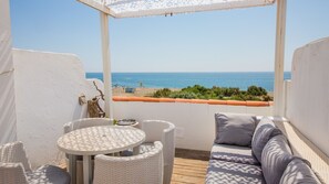 A balcony with wicker furniture, a table, and a view of the sea. - Aldea Beach Townhouse 153 (Manilva)