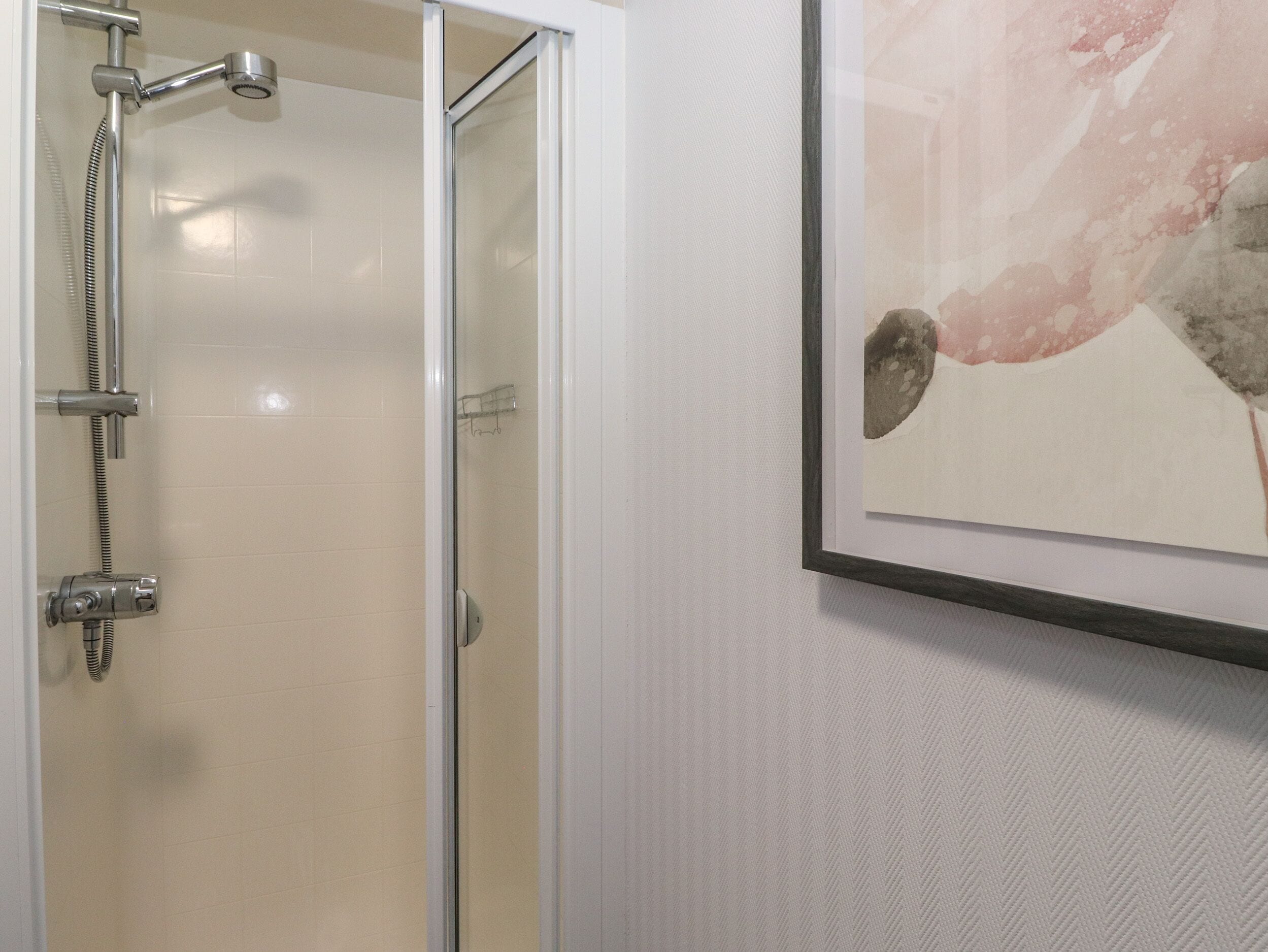 A bathroom with a glass shower enclosure, a framed artwork on the wall, and a towel rack.
