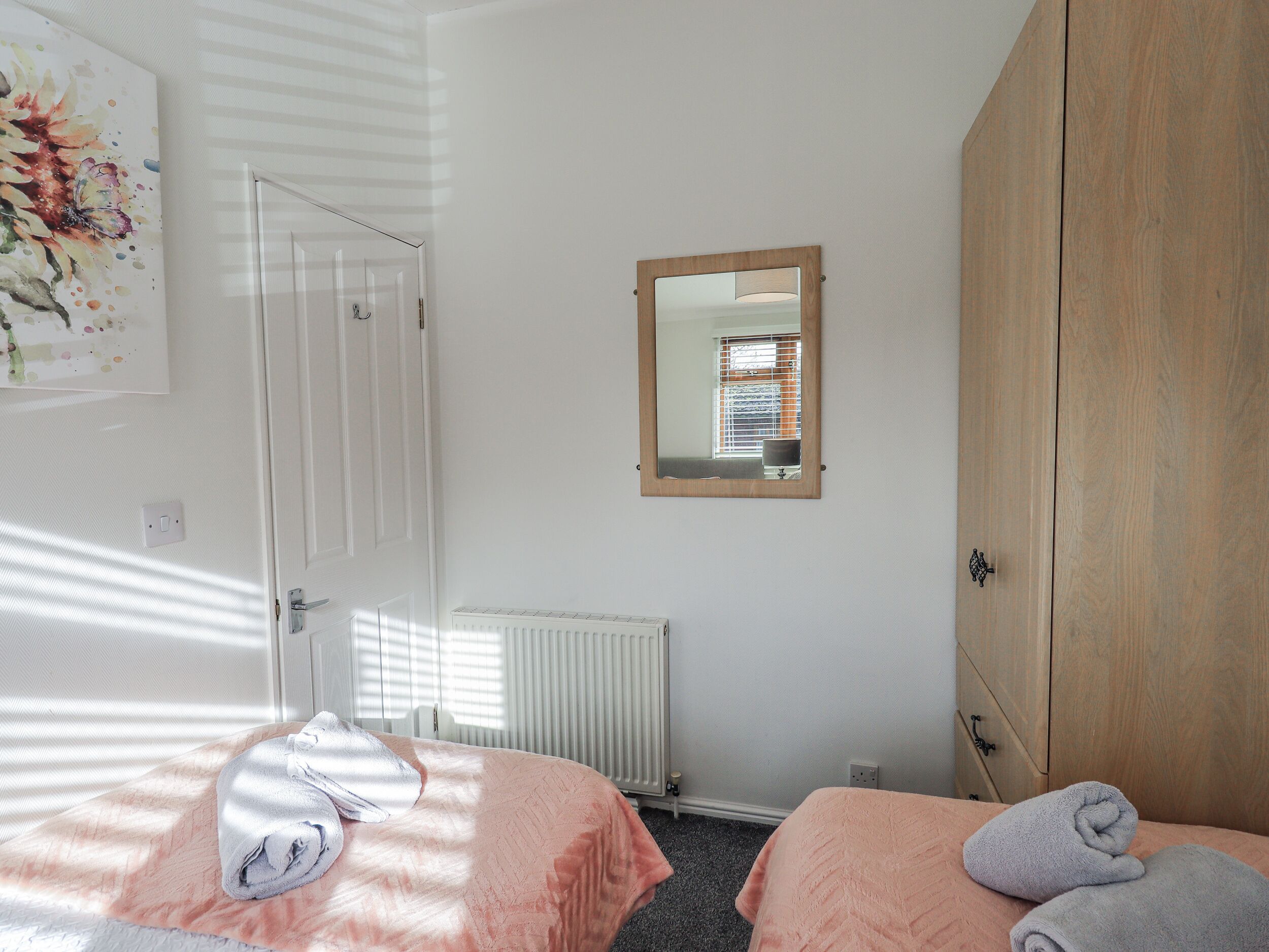 A bedroom with two beds, a radiator, a wooden wardrobe, and a mirror on the wall.