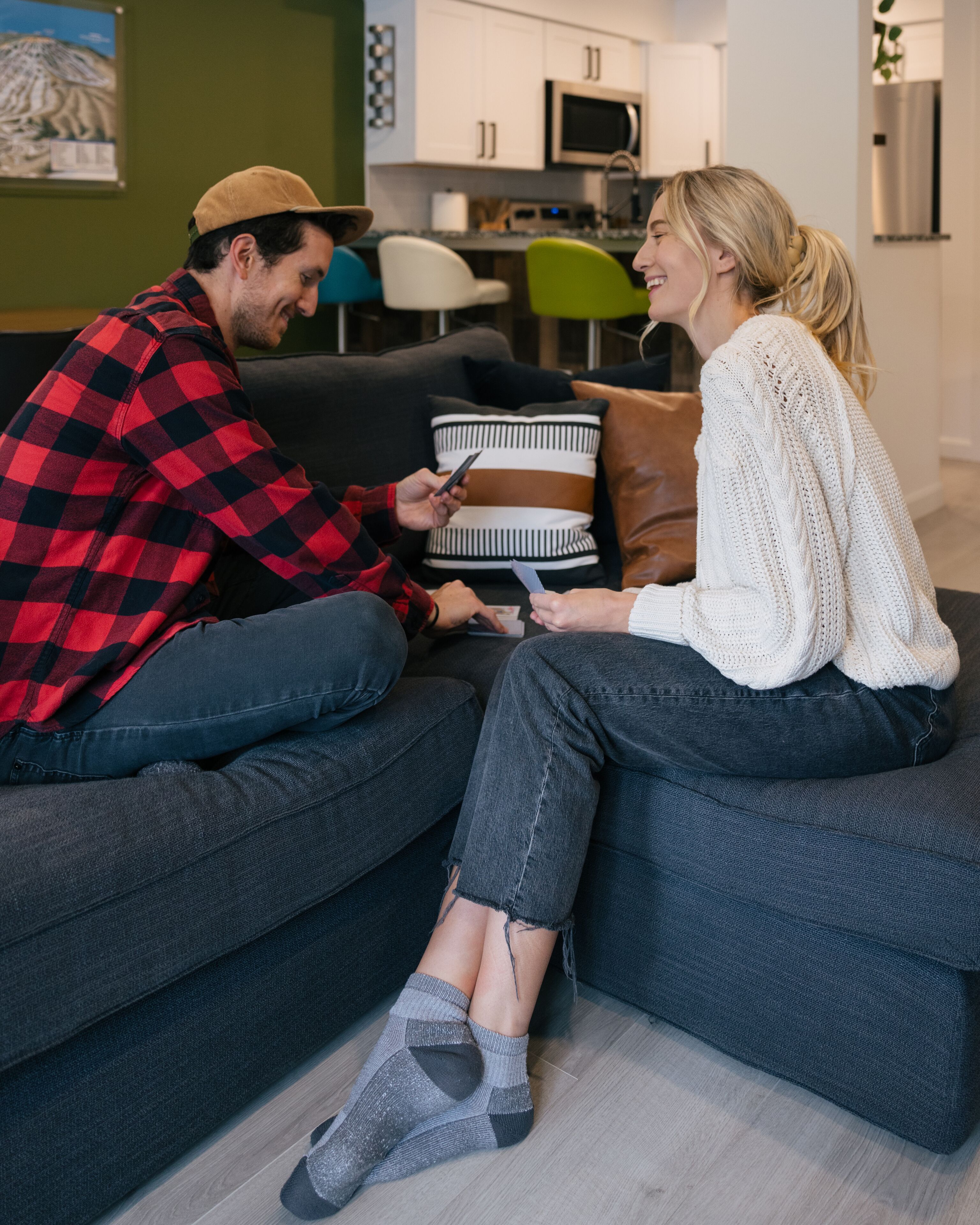 Un couple est assis sur un canapé d’angle dans un salon moderne, avec une cuisine en arrière-plan.