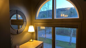 A room with a large arched window, a wall-mounted mirror, a wooden dresser, and a table lamp. - Modern Mount Snow Gnarvana - Balcony, Loft, Pets, Hiking (Dover)
