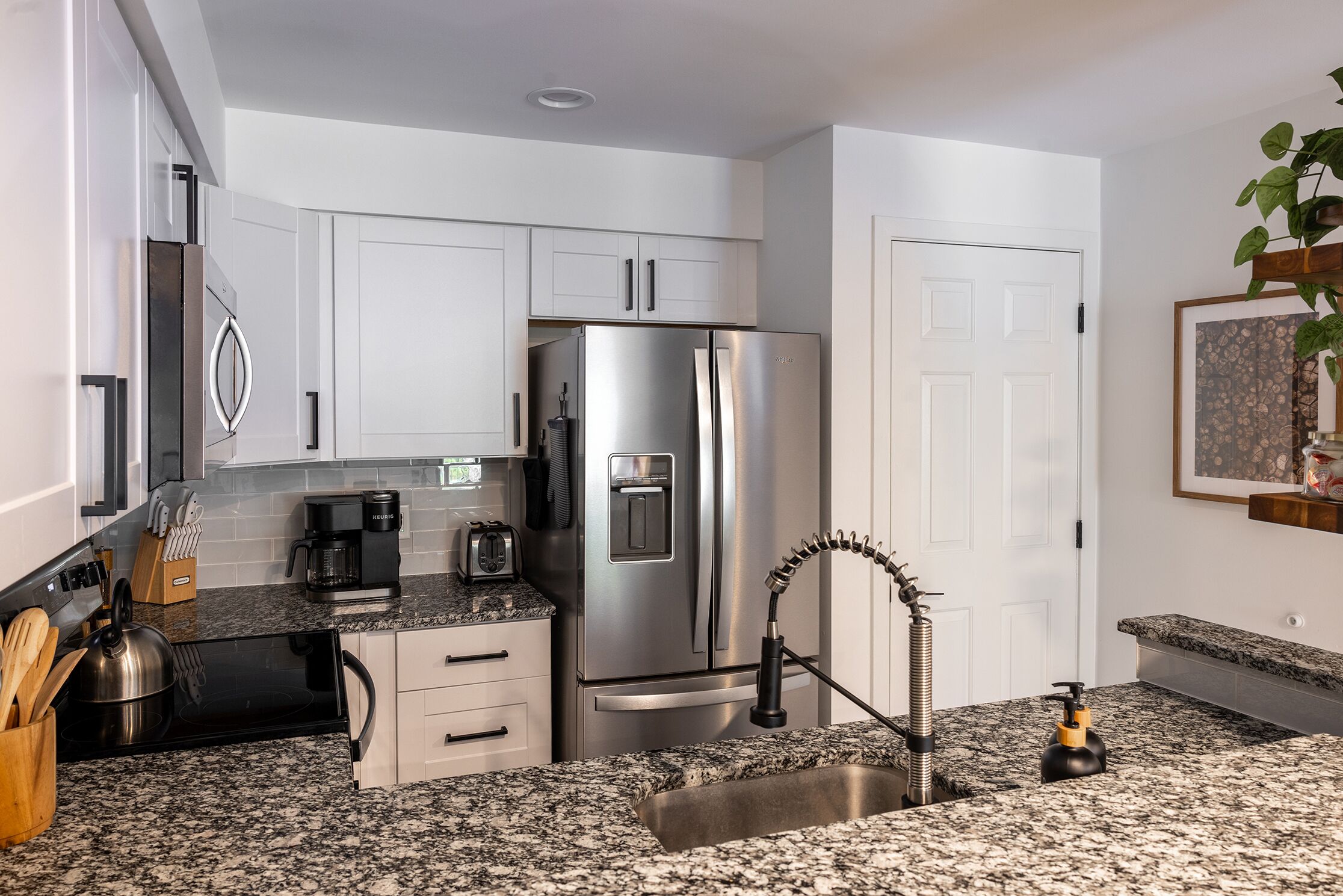 A modern kitchen with white cabinets, stainless steel appliances, granite countertops, and a built-in sink.