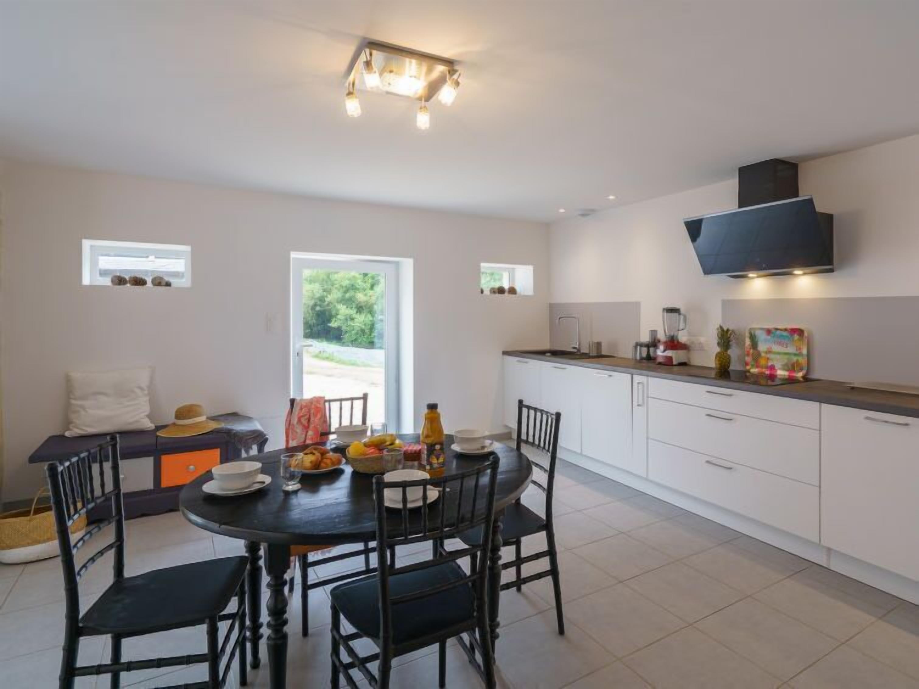A modern kitchen with white cabinets, a black range hood, and a dining area with a round table and chairs.