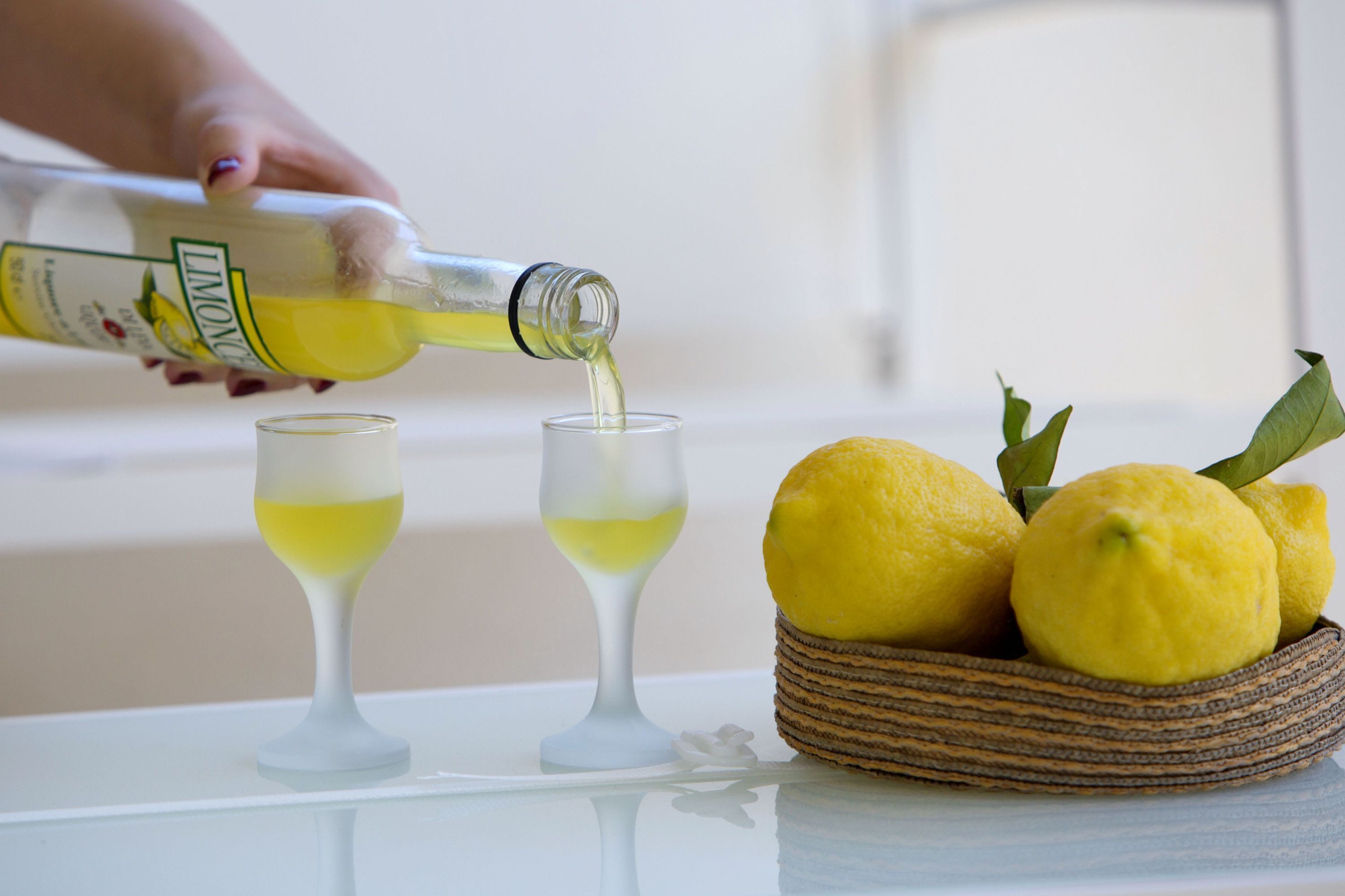 Une bouteille de limonade est versée dans deux verres, avec des citrons dans un panier à côté.