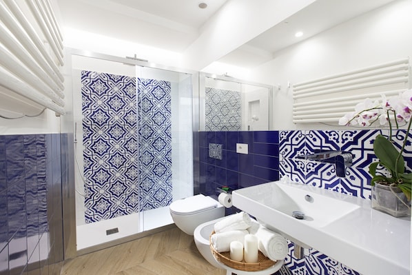A bathroom with patterned tiles, a white sink, a toilet, and a shower with a glass door.
