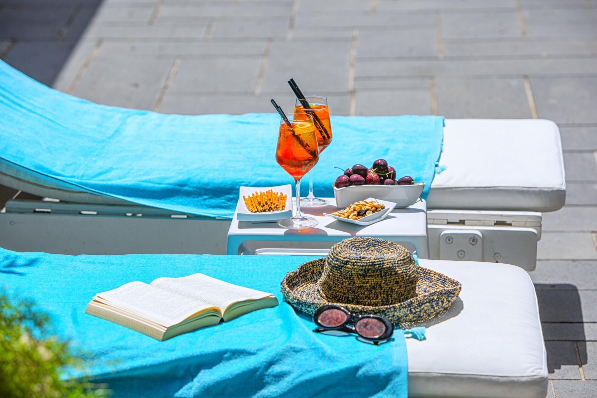 A sun lounger with a blue towel, a book, a hat, and a glass of drink with a straw.