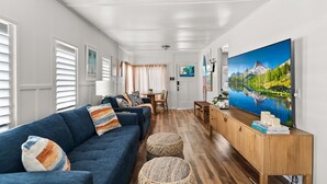 Una sala de estar moderna con un sofá azul, piso de madera, un televisor grande y un cuadro de un lago.