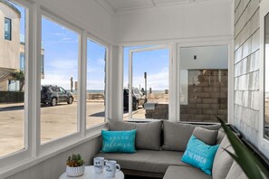 A sunroom with large windows overlooking a beach, a cushioned seating area, and a small table with a plant and two mugs. - Newly Updated! - Oceanview Sea Gem Cottage- Bikes/ Boards,10 sec walk to beach (Newport Beach)