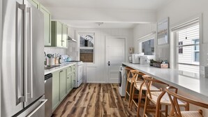 Una cocina moderna con armarios blancos, piso de madera y una barra con taburetes.