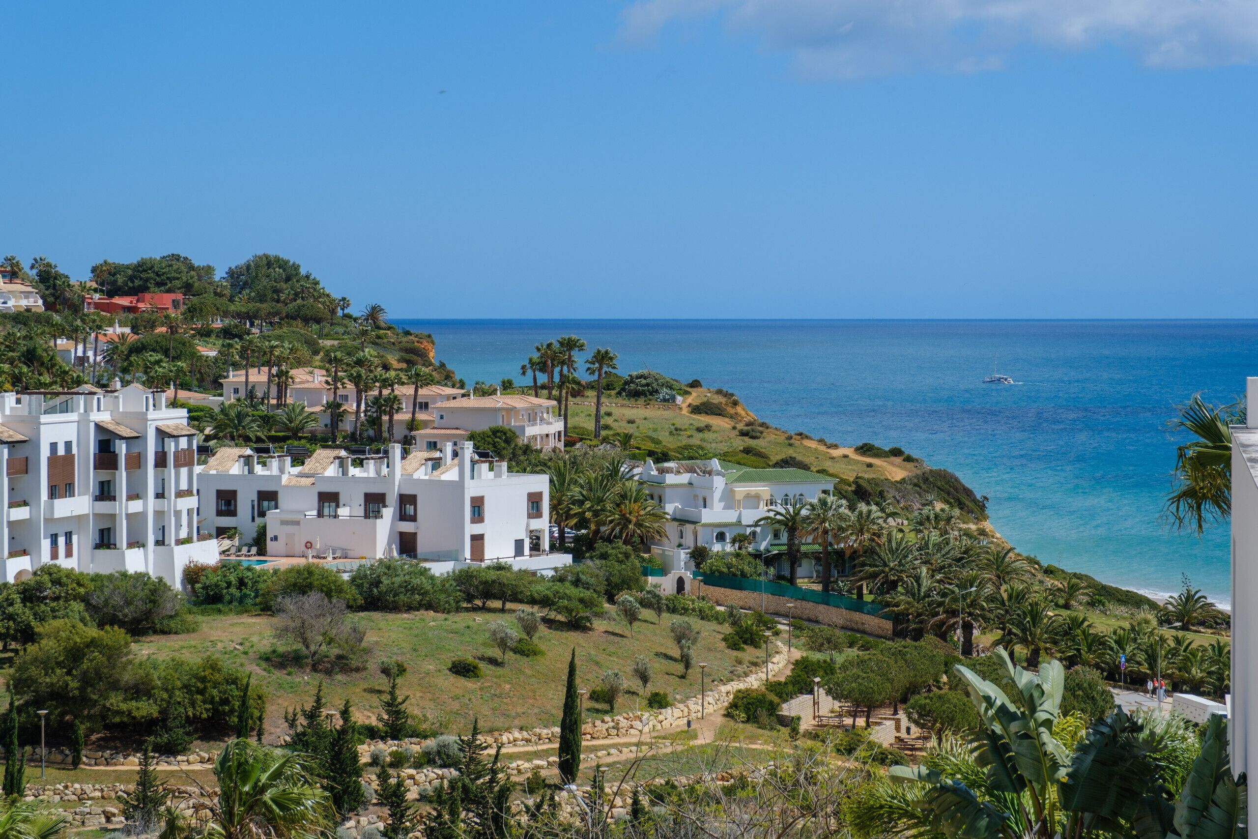 Un quartier résidentiel en bord de mer, avec des bâtiments modernes, une vue dégagée sur la mer et un aménagement paysager bien entretenu, agrémenté d’arbres et d’arbustes.