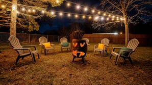 Un jardin avec des fauteuils Adirondack, un foyer et des guirlandes lumineuses.