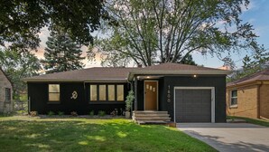 Une maison moderne à deux étages, avec une façade sombre, un garage et une pelouse bien entretenue.