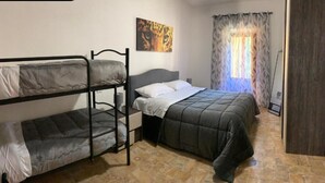 A room with bunk beds, a single bed, a painting on the wall, and a window with curtains. - Residence the garden on the Nera river - apt2 (Borgo Cerreto)