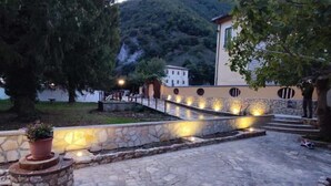 A stone-paved courtyard with a stone wall, a potted plant, and a building with a stone facade and windows. - Residence the garden on the Nera river - apt2 (Borgo Cerreto)