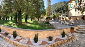 A stone pathway leading to a building with a curved stone wall and small potted plants. - Residence the garden on the Nera river - apt2 (Borgo Cerreto)