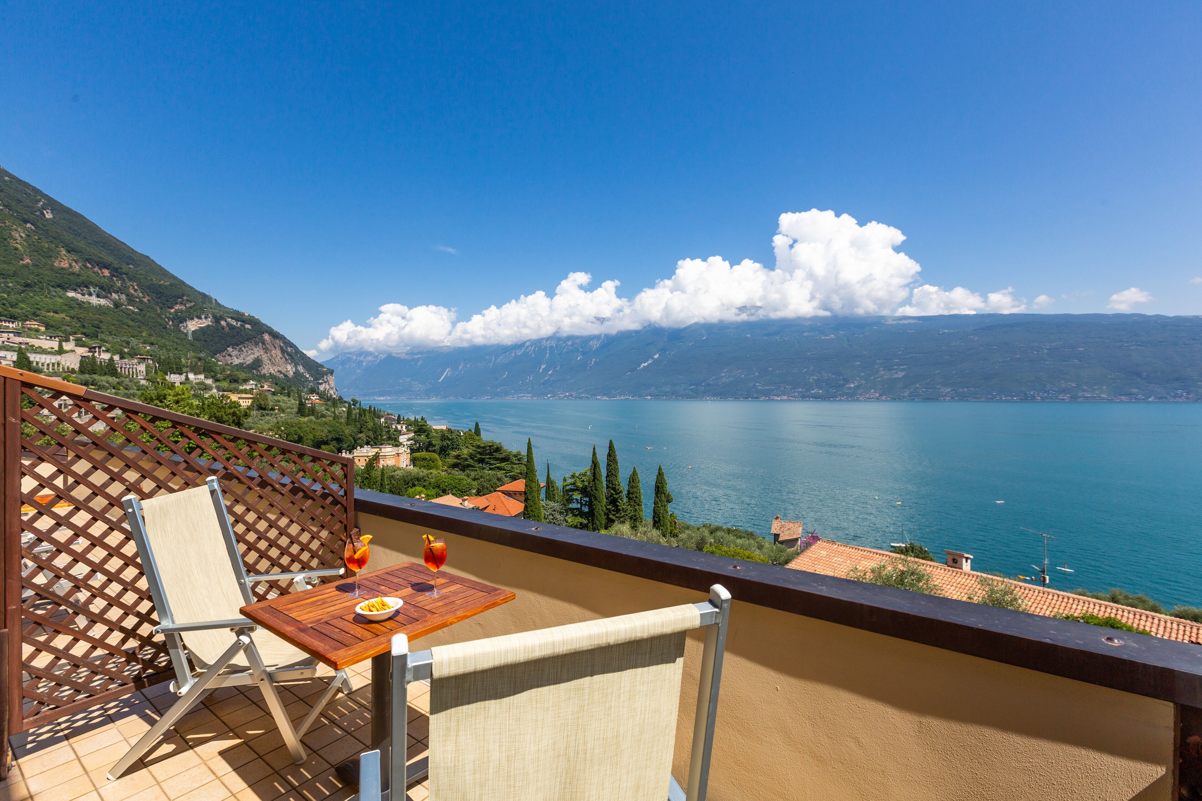 A balcony with a table, chair, and a scenic view of a lake and mountains.