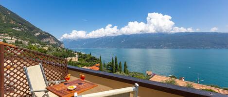 A balcony with a table, chair, and a scenic view of a lake and mountains.